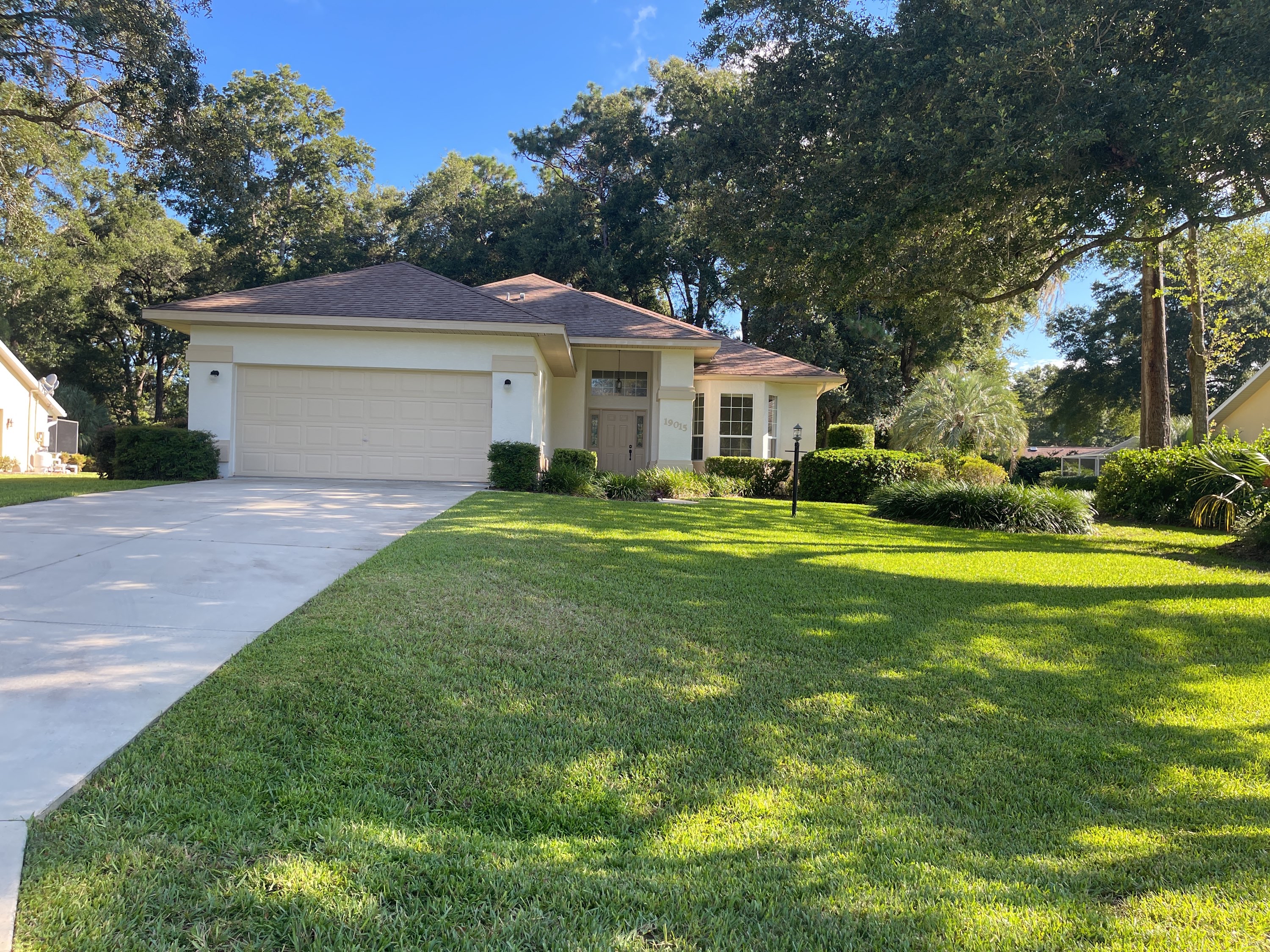 Clean beige stucco home with wide bright green lawn and clean driveway in afternoon light