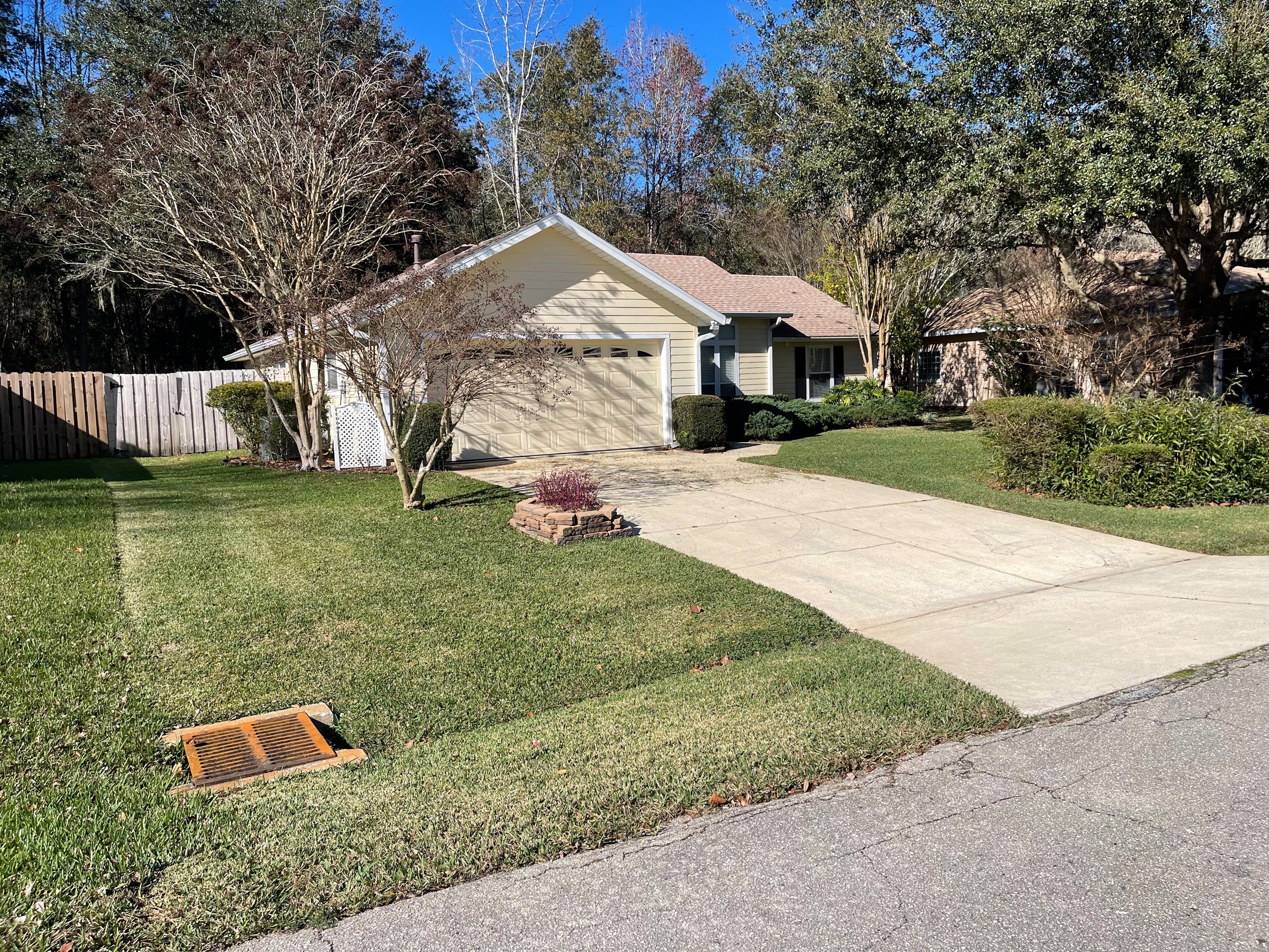 Neat residential front yard with manicured shrubs, driveway, and brick planter