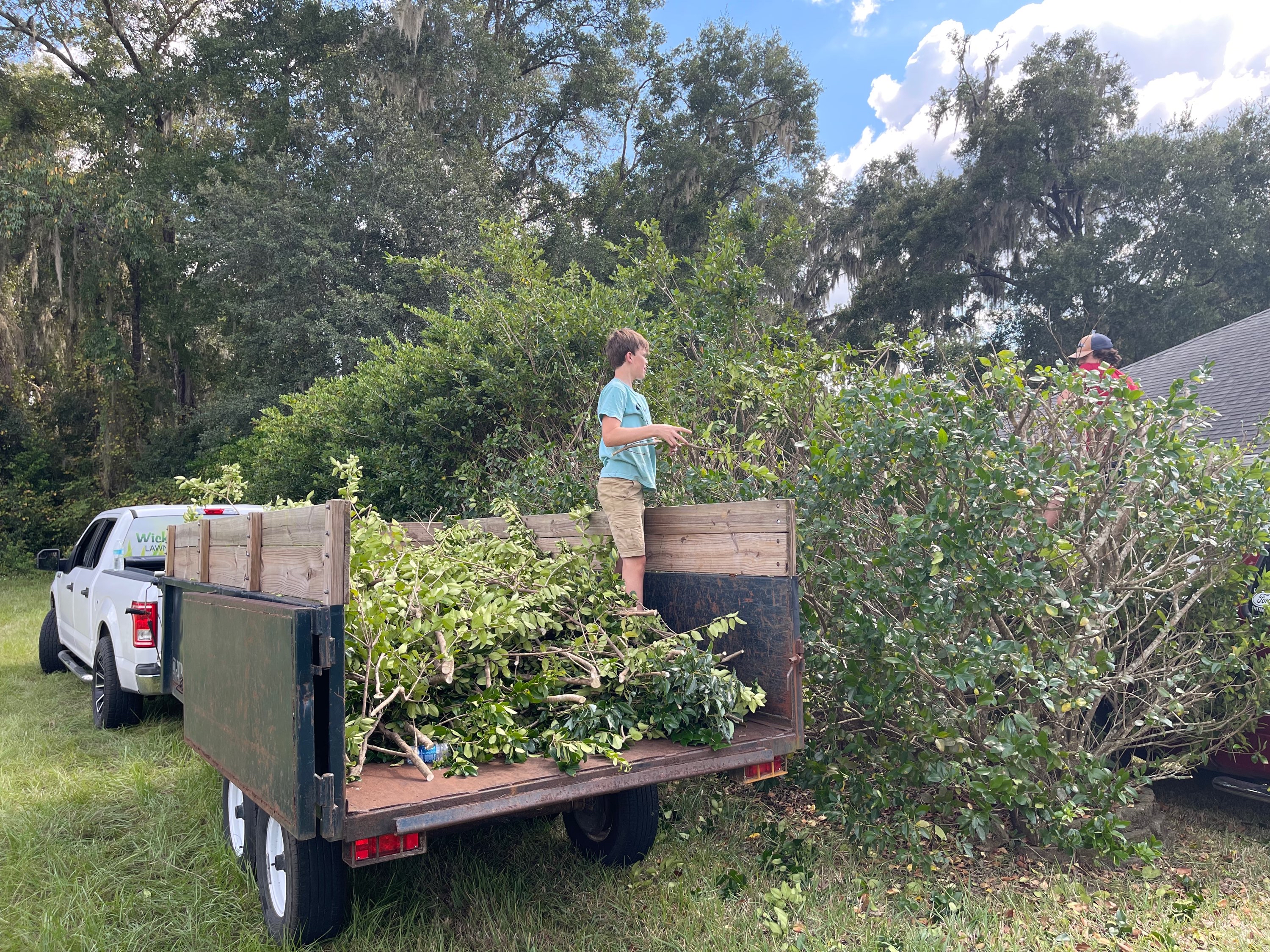 Two crew members loading brush and debris into a trailer