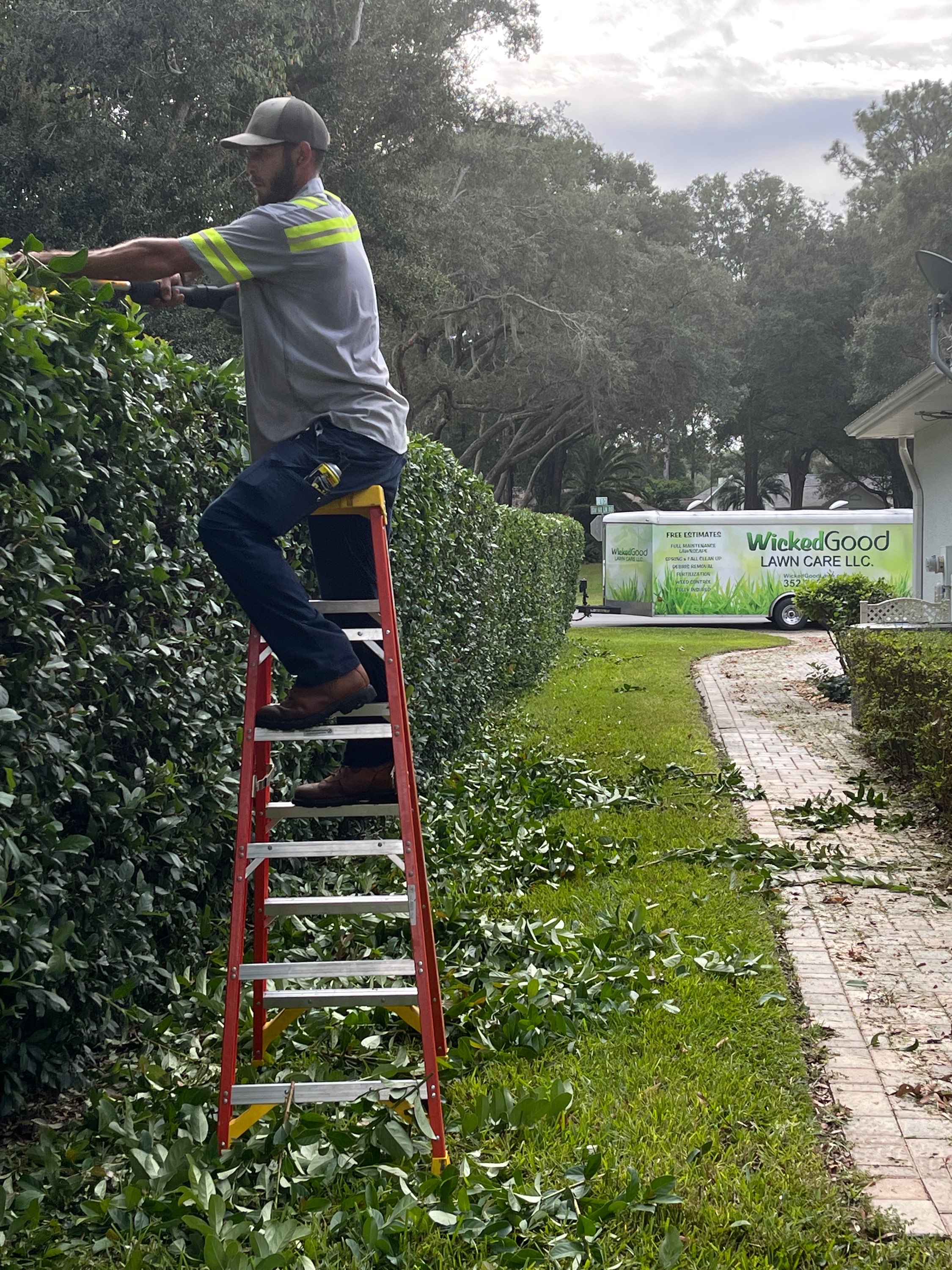 Crew member on tall ladder working at height with WGLC trailer visible